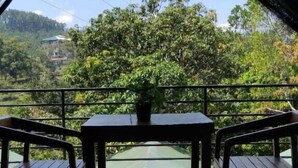 Una stanza con un letto, un tavolo e delle sedie, affacciata su un paesaggio verdeggiante con alberi e colline.