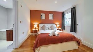 Een slaapkamer met een groot bed, twee bedlampen, een raam met gordijnen en uitzicht op een gebouw.