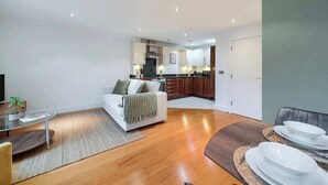 Een moderne woonkamer met een bank, een glazen salontafel en een eethoek met borden en bestek.