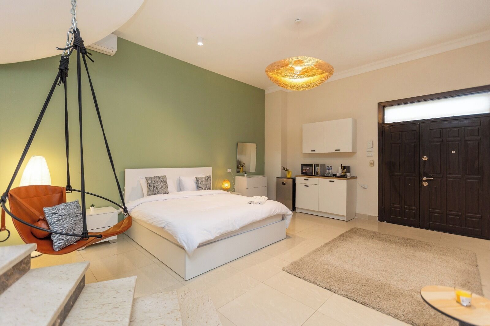 A bedroom with a bed, a hanging chair, a desk, a wardrobe, and a door.