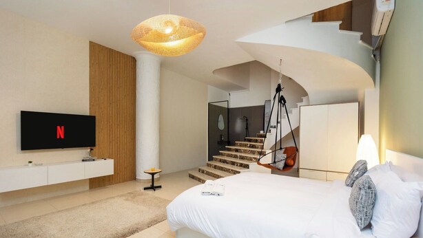 A modern bedroom with a large bed, a TV mounted on the wall, a hanging chair, and a staircase leading to an upper level. - Host Prime Boutique Hotel 01 (New Cairo)