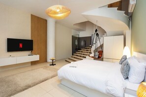 A modern bedroom with a large bed, a TV mounted on the wall, a hanging chair, and a staircase leading to an upper level. - Host Prime Boutique Hotel 01 (New Cairo)