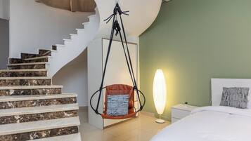 Ein modernes Hotelzimmer mit einer Marmortreppe, einem Hängekorbstuhl, einer Nachttischlampe und einem Bett mit weißem Kopfteil.