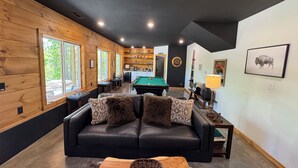 A cozy living room with a black leather sofa, a pool table, and a dining area with wooden walls and a kitchen in the background. - Beautiful 2-Bedroom Getaway in Marble Falls: Hike, Float, Unwind in the Ozarks (Marble Falls)