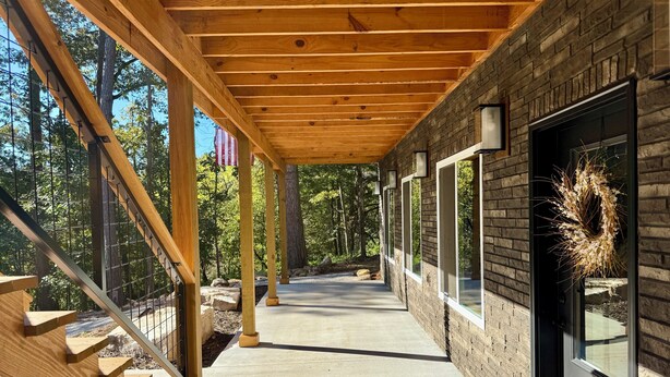 A covered wooden deck with a concrete pathway leading to a door with a wreath. - Beautiful 2-Bedroom Getaway in Marble Falls: Hike, Float, Unwind in the Ozarks (Marble Falls)