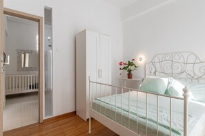 A bedroom with a white bed, a white wardrobe, a white crib, and a mirror with a decorative frame. - Apartment 'Unique Stays in Athens' with Shared Terrace, Wi-Fi and Air Conditioning (Kallithea)