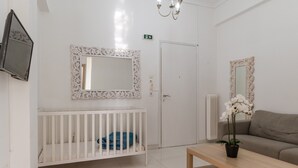 A room with a crib, a sofa, a wooden table, a mirror, and a television. - Apartment 'Unique Stays in Athens' with Shared Terrace, Wi-Fi and Air Conditioning (Kallithea)