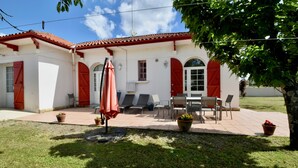 Un bâtiment doté d’un toit en tuiles, de volets rouges et d’une terrasse aménagée avec du mobilier d’extérieur.