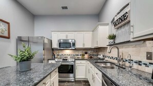 Eine moderne Küche mit weißen Schränken, Granit-Arbeitsplatten, Edelstahlgeräten und einer Rückwand mit einem Mosaikfliesenmuster.