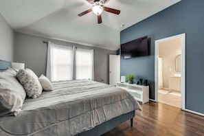 A bedroom with a bed, a ceiling fan, a TV mounted on the wall, and a door leading to a bathroom. - 3BD Home  Garage  HWY 360  Grand Prairie (GP020) (Grand Prairie)