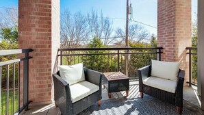 A balcony with wicker furniture, a small table, and a view of trees and power lines. - 3BD  Pool Table Dallas Dallas DAL212 (Dallas)