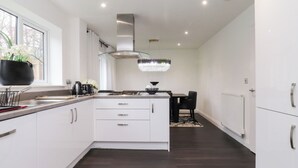 A modern kitchen with white cabinets, a gas stove, and a dining area with a chandelier. - Mellings Place (Carnforth)