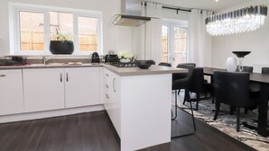 A modern kitchen with white cabinetry, a central island, and a dining area with black chairs. - Mellings Place (Carnforth)