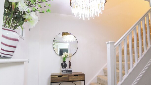 A staircase with a white railing, a wooden console table with a mirror, and a vase with flowers. - Mellings Place (Carnforth)