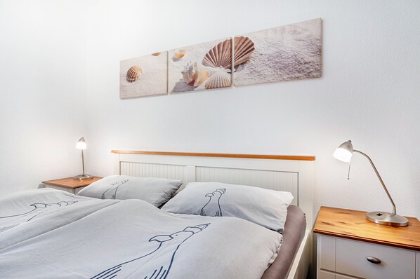 Un dormitorio con una cama, dos mesitas de noche, una lámpara y una obra de arte en la pared.