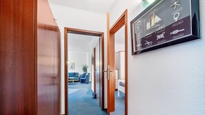 A hallway with wooden doors, a framed nautical-themed display, and a glimpse of a living area with furniture.