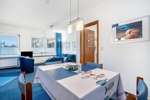 Un comedor con una mesa preparada para cuatro personas, un sofá azul y un cuadro en la pared.