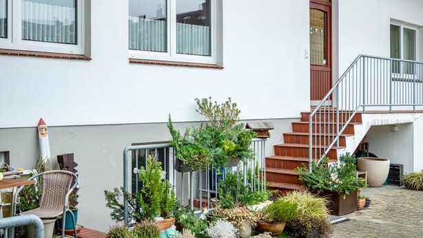 A white building with a staircase, potted plants, and a chair.