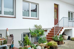 Een wit gebouw met een trap, plantenpotten en een stoel.