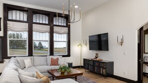 Uma sala de estar moderna com um sofá seccional, uma mesa de centro com uma planta, uma estante e uma TV de tela plana na parede.