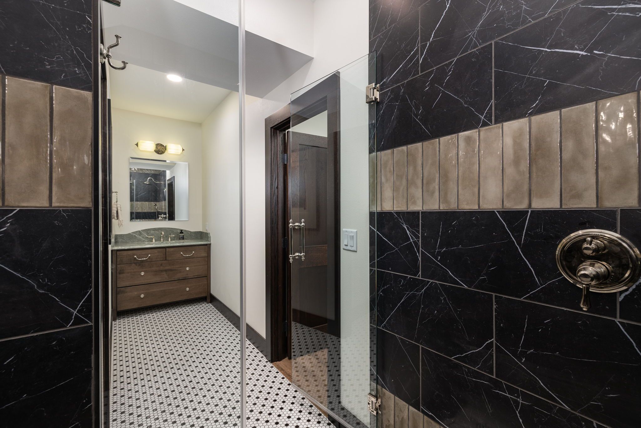 A modern bathroom with black marble walls, a glass shower enclosure, and a wooden vanity with a mirror.