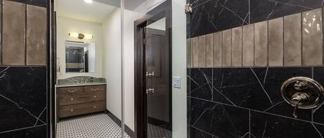A modern bathroom with black marble walls, a glass shower enclosure, and a wooden vanity with a mirror.