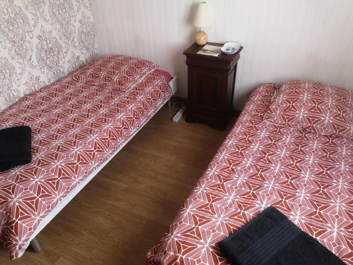 A room with two single beds, a small wooden nightstand with a lamp, and a patterned wall.
