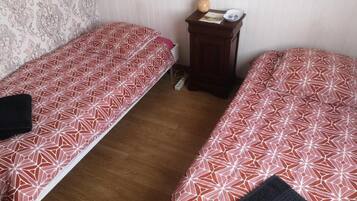 A room with two single beds, a small wooden nightstand with a lamp, and a patterned wall.