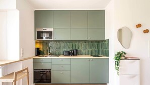 A compact kitchen with teal cabinets, a built-in oven, and a sink. - Studio terrace in the center of town (Luxembourg)