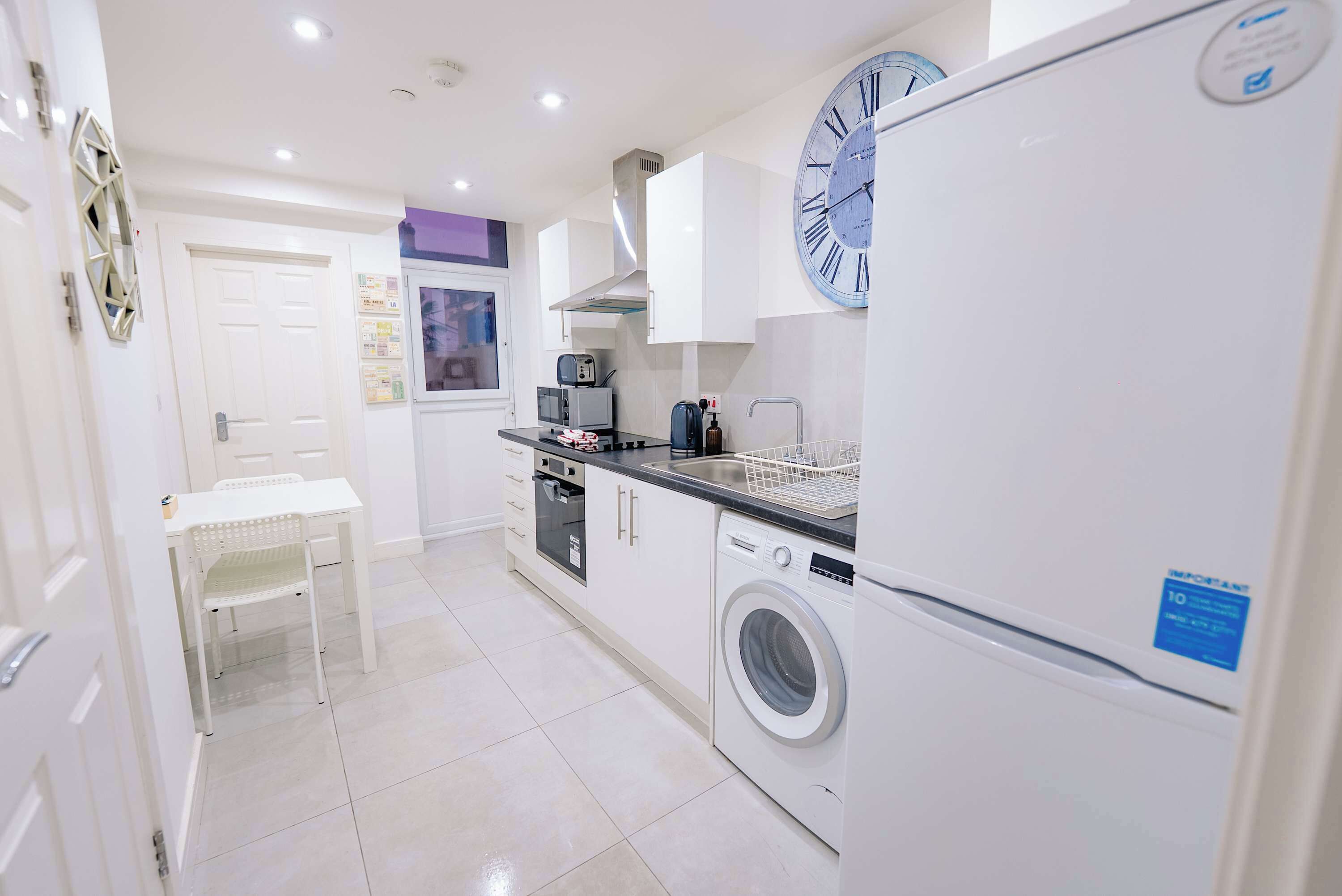 A compact kitchen with a washing machine, a microwave, and a clock on the wall.