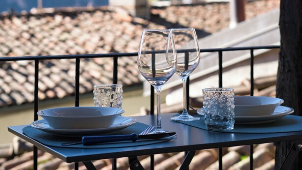 A table set for two with wine glasses and a bowl, overlooking a mountainous landscape and a bell tower. - Lòbia in via Parrochiale - app. Legno (P2) (Barzio)