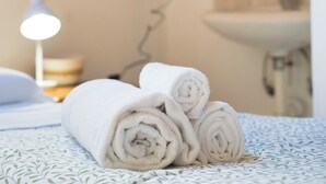 A neatly made bed with rolled white towels, a bedside lamp, and a bathroom visible in the background. - Lòbia in via Parrochiale - app. Legno (P2) (Barzio)