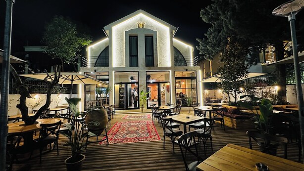 An outdoor dining area with wooden tables and chairs, a patterned rug, and potted plants. - Villa Garden Boutique Hotel Tirana (Tirana)