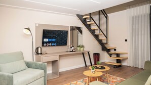 A modern living room with a sofa, a coffee table, a TV mounted on the wall, a staircase, and a kitchen area. - Villa Garden Boutique Hotel Tirana (Tirana)