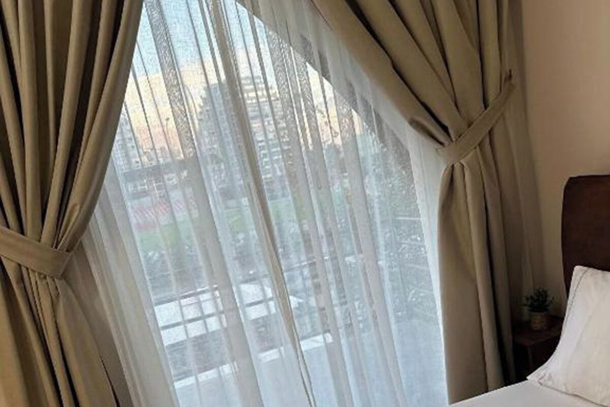 A hotel room with a bed, a nightstand, and a window with curtains.