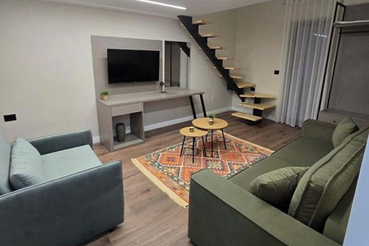A modern living room with a flat-screen TV, two sofas, a coffee table, and a staircase.