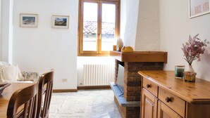 A dining area with a wooden table and chairs, a brick fireplace, and a window with a view of a mountain. - Lòbia in via Parrochiale - app. Pietra (P1) (Barzio)