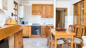A kitchen with wooden cabinets, a stove, and a dining table with chairs. - Lòbia in via Parrochiale - app. Pietra (P1) (Barzio)
