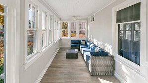 Eine überdachte Veranda mit einer langen Bank und einem Ecksofa, großen Fenstern und Blick ins Freie.