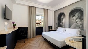 Una habitación de hotel con cama, escritorio, silla, televisor y ventana con cortinas.
