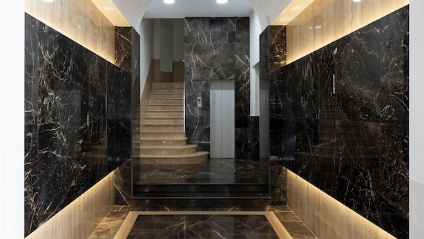 Un interior moderno con una escalera de mármol, un ascensor de vidrio y un diseño elegante y minimalista.