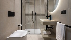 Un baño moderno con cabina de ducha de vidrio, inodoro, lavamanos y espejo.