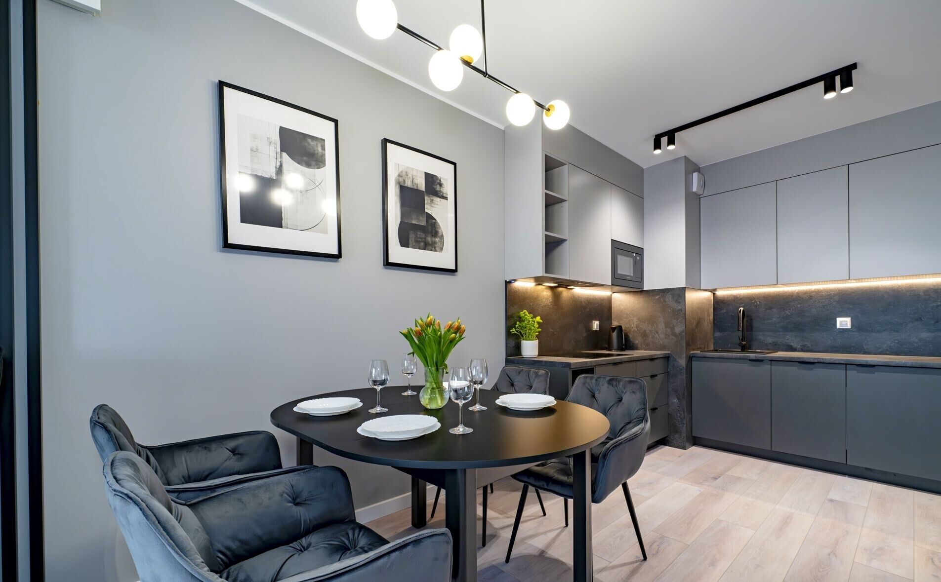 A modern kitchen with grey cabinets, a dining area with a round table and chairs, and two framed abstract artworks on the wall.