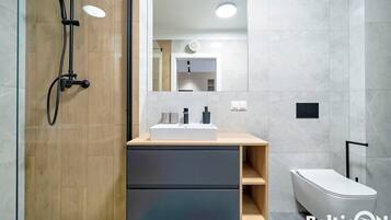 A modern bathroom with a wooden vanity, a white sink, and a shower with a handheld showerhead.