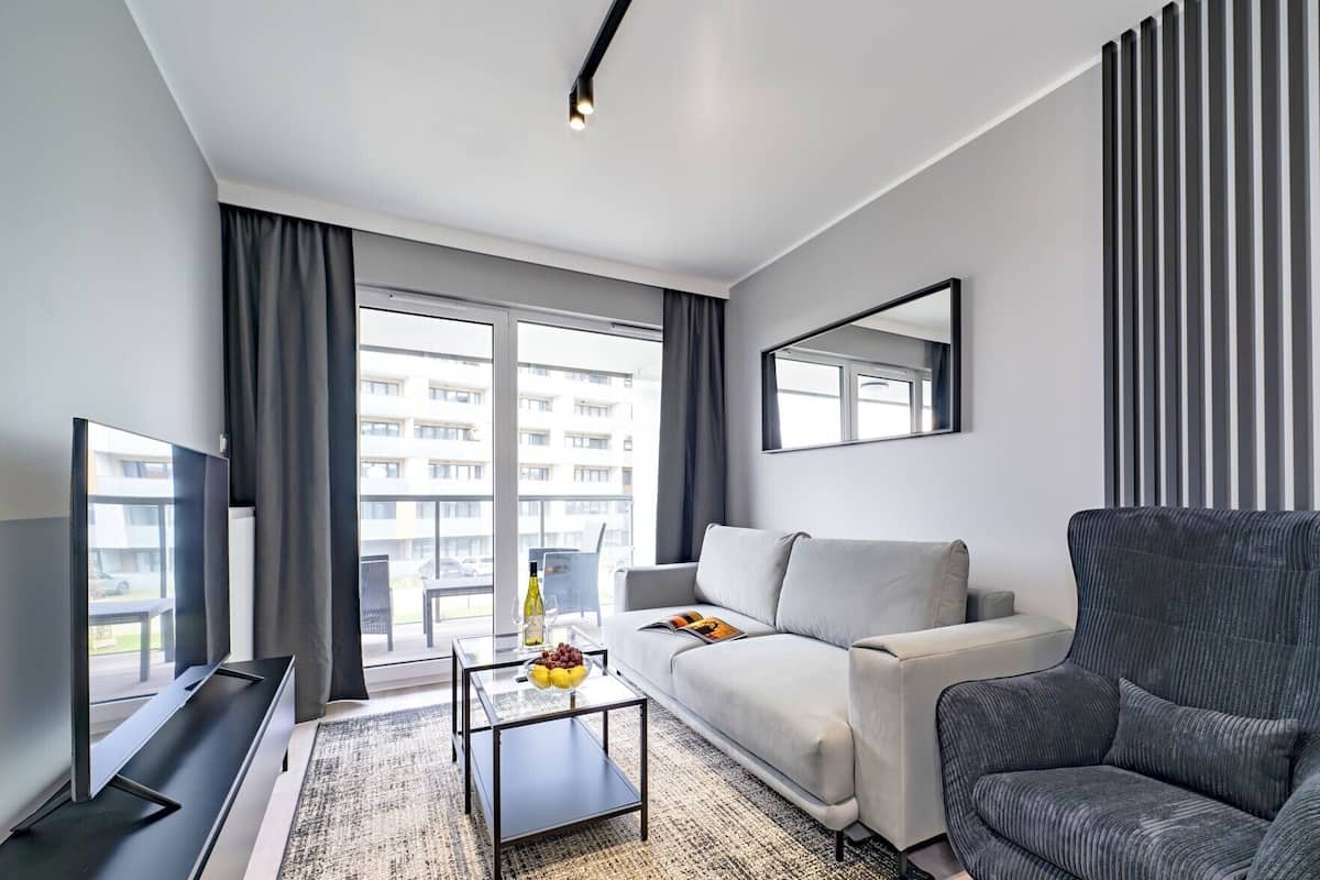 A modern living room with a sofa, armchair, TV, and a glass coffee table with a bowl of fruit.
