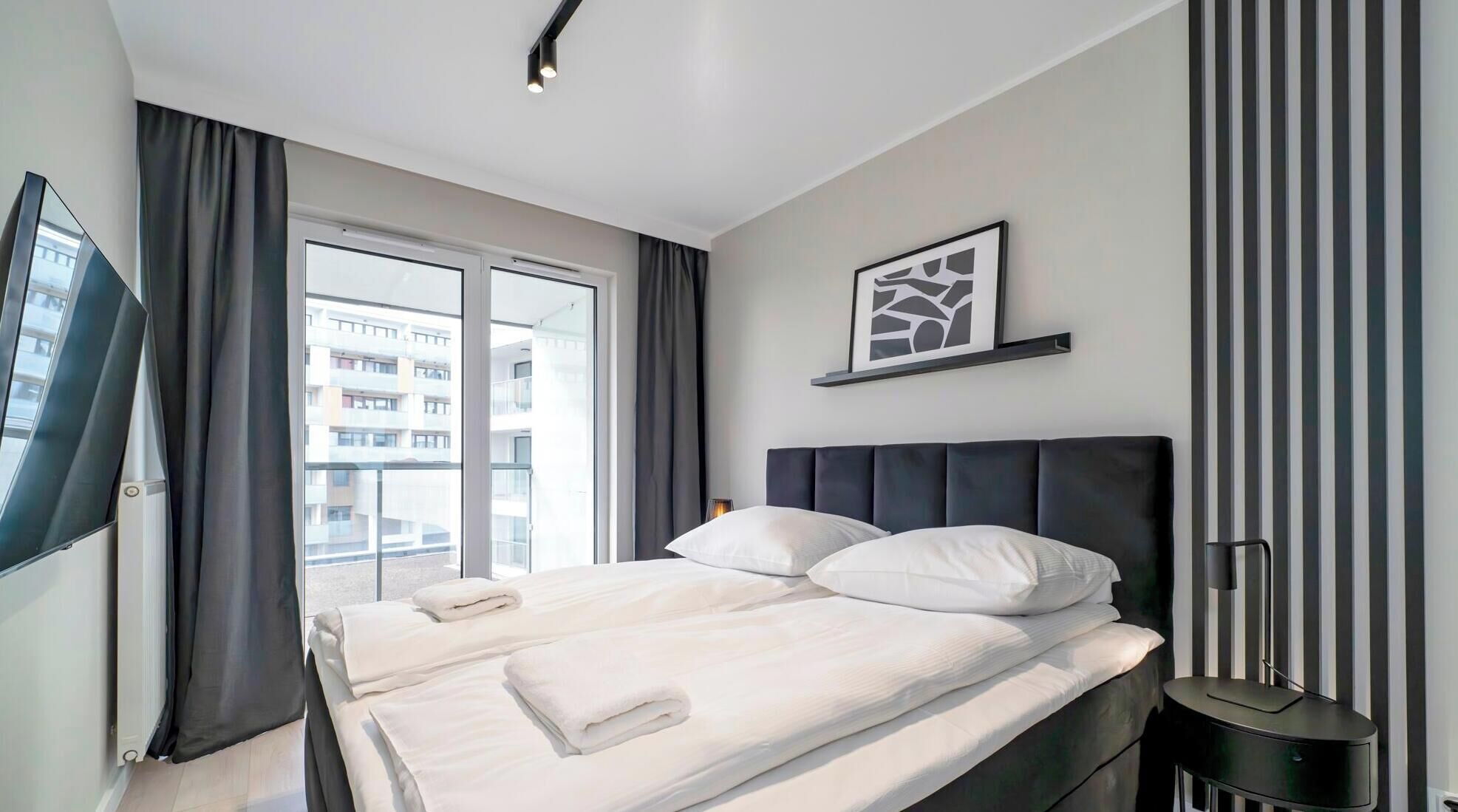 A modern hotel room with a large bed, a flat-screen TV, and a view of the city through the window.