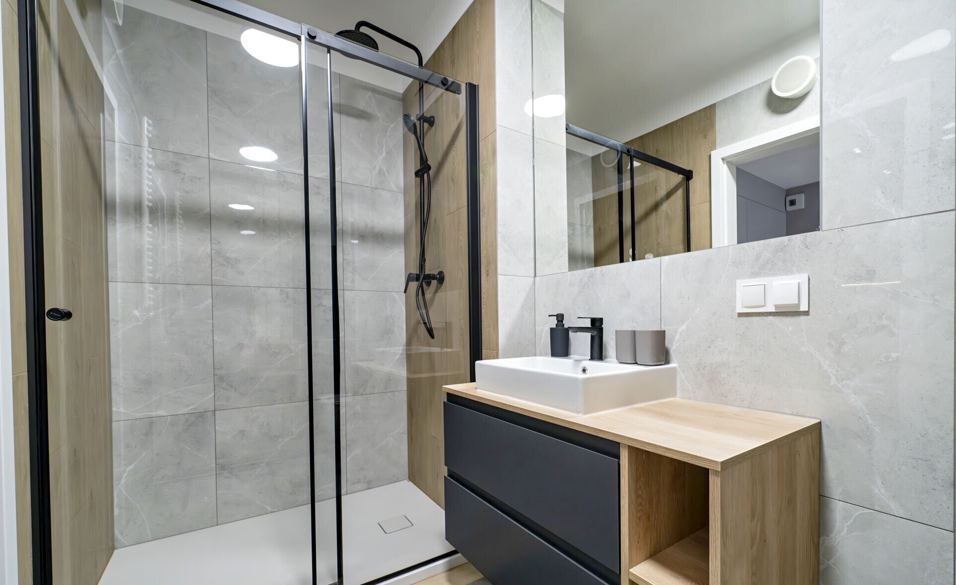 A modern bathroom with a glass shower enclosure, a white sink, and a mirror.