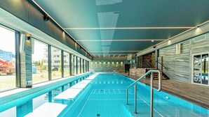 A modern indoor swimming pool with clear glass walls, a wooden deck, and a view of the outside. - BalticON Apartments Kasprowicza (Kolobrzeg)