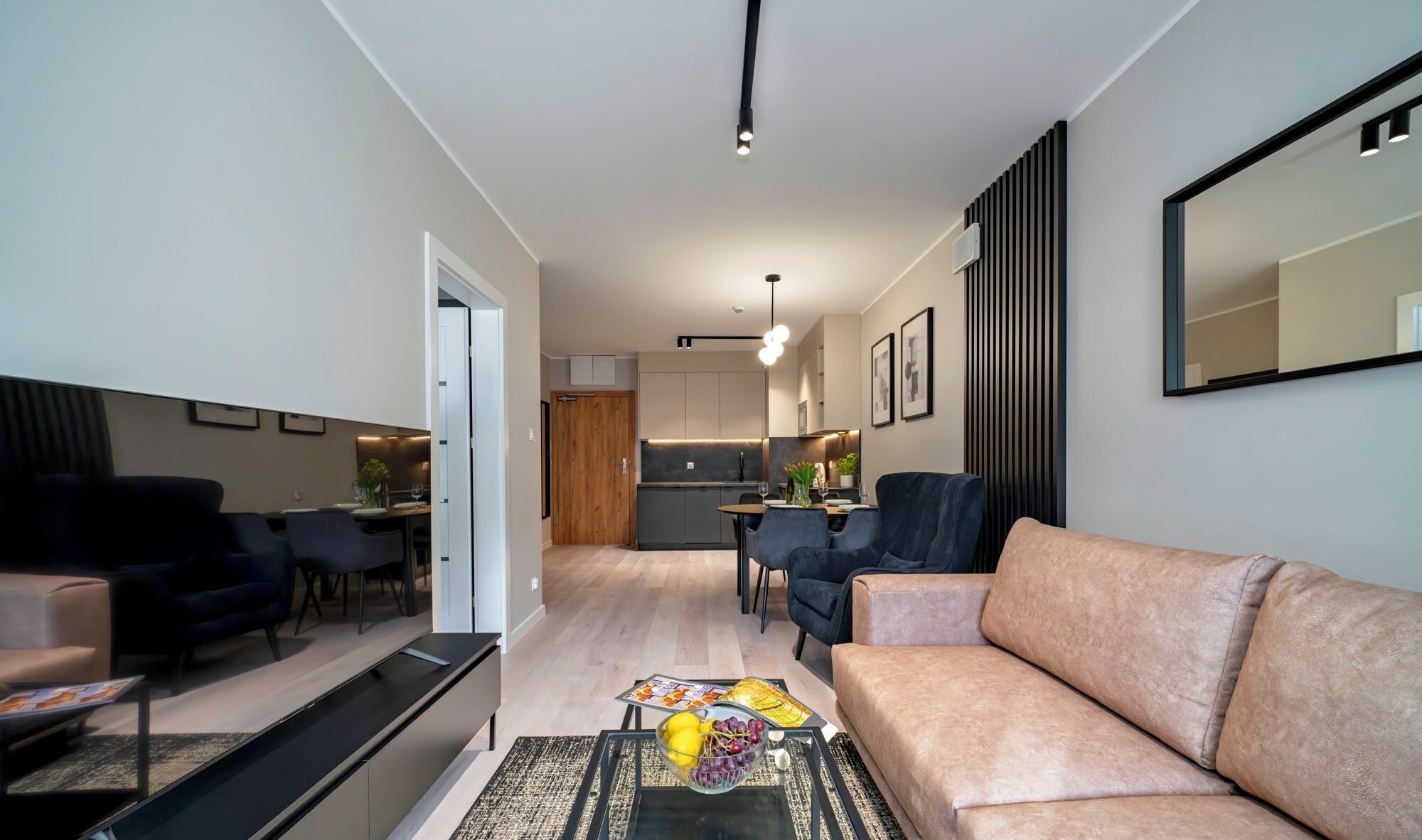 A modern living room with a sofa, a coffee table with fruit, and a dining area with chairs and a table.