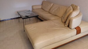 Un canapé en cuir beige avec une structure en bois, une table basse en verre et un petit tableau encadré accroché au mur.